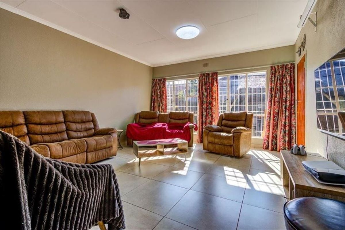 A spacious living room featuring large windows with security bars, tiled flooring, and an installed air conditioning unit.