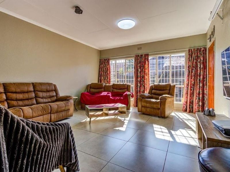 A spacious living room featuring large windows with security bars, tiled flooring, and an installed air conditioning unit.