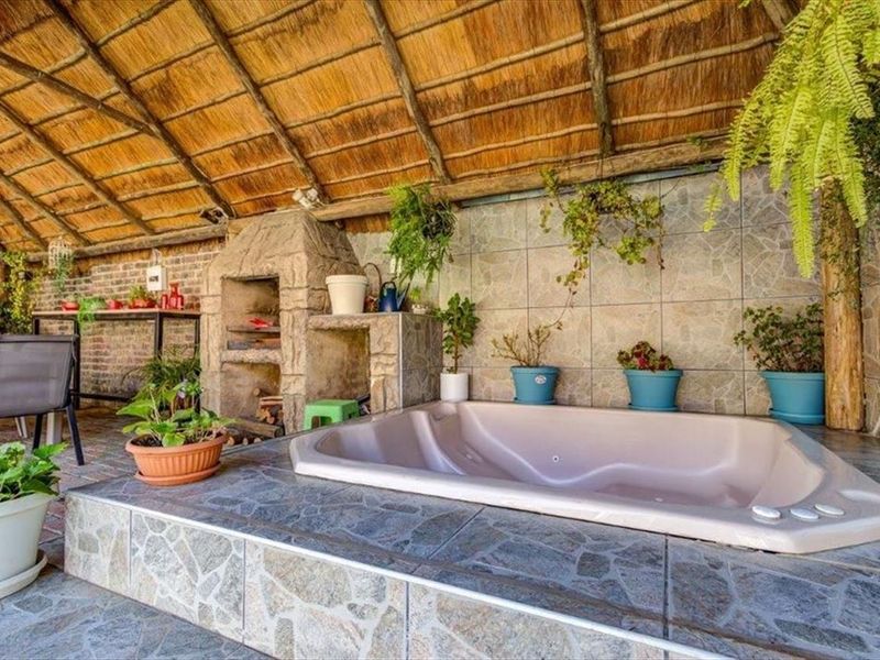 Covered outdoor patio area featuring a thatched roof, built-in braai, and a sunken spa bath with stone-tiled finishes.