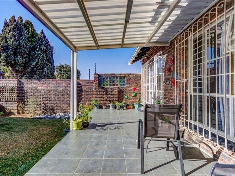 A covered patio area with tiled flooring, brick boundary walls, and security bars on the windows, overlooking a small garden space.