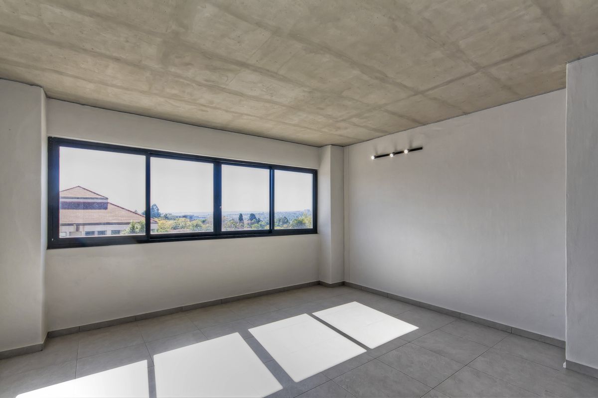 A bright, empty living area featuring an exposed concrete ceiling, large windows with scenic views, and modern tiled flooring.