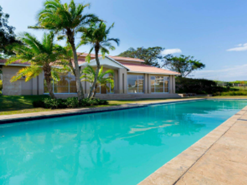 A well-maintained swimming pool area featuring a large pool, tiled decking, and a view of the property's exterior facade.