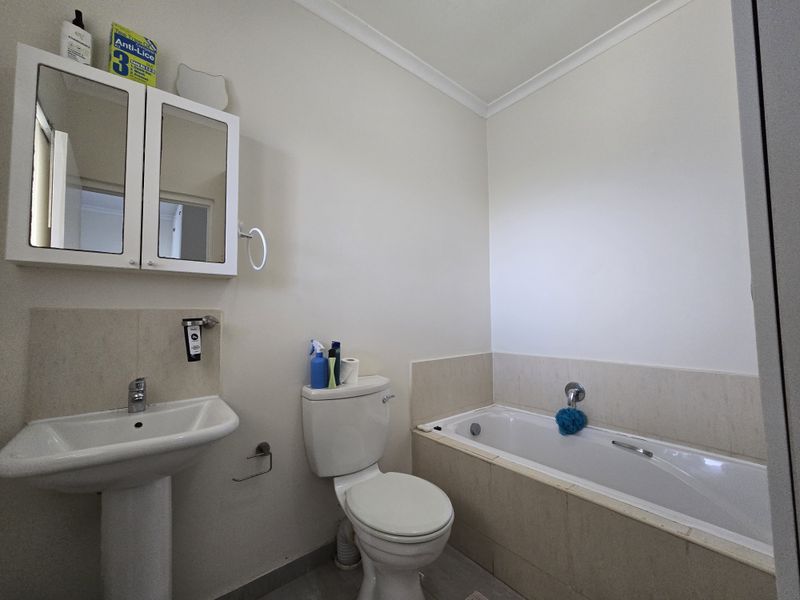 A functional bathroom featuring a pedestal basin, toilet, and a tiled bathtub with a mirrored medicine cabinet.
