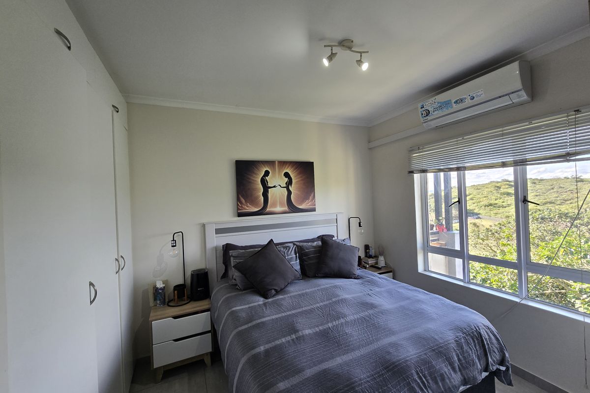 A well-maintained bedroom featuring built-in wardrobes, a split-system air conditioner, and large windows with venetian blinds offering natural light and scenic views.