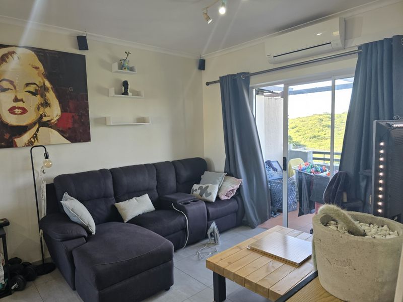 A comfortable living room featuring tiled flooring, a wall-mounted air conditioning unit, and large sliding glass doors providing access to an outdoor balcony area.