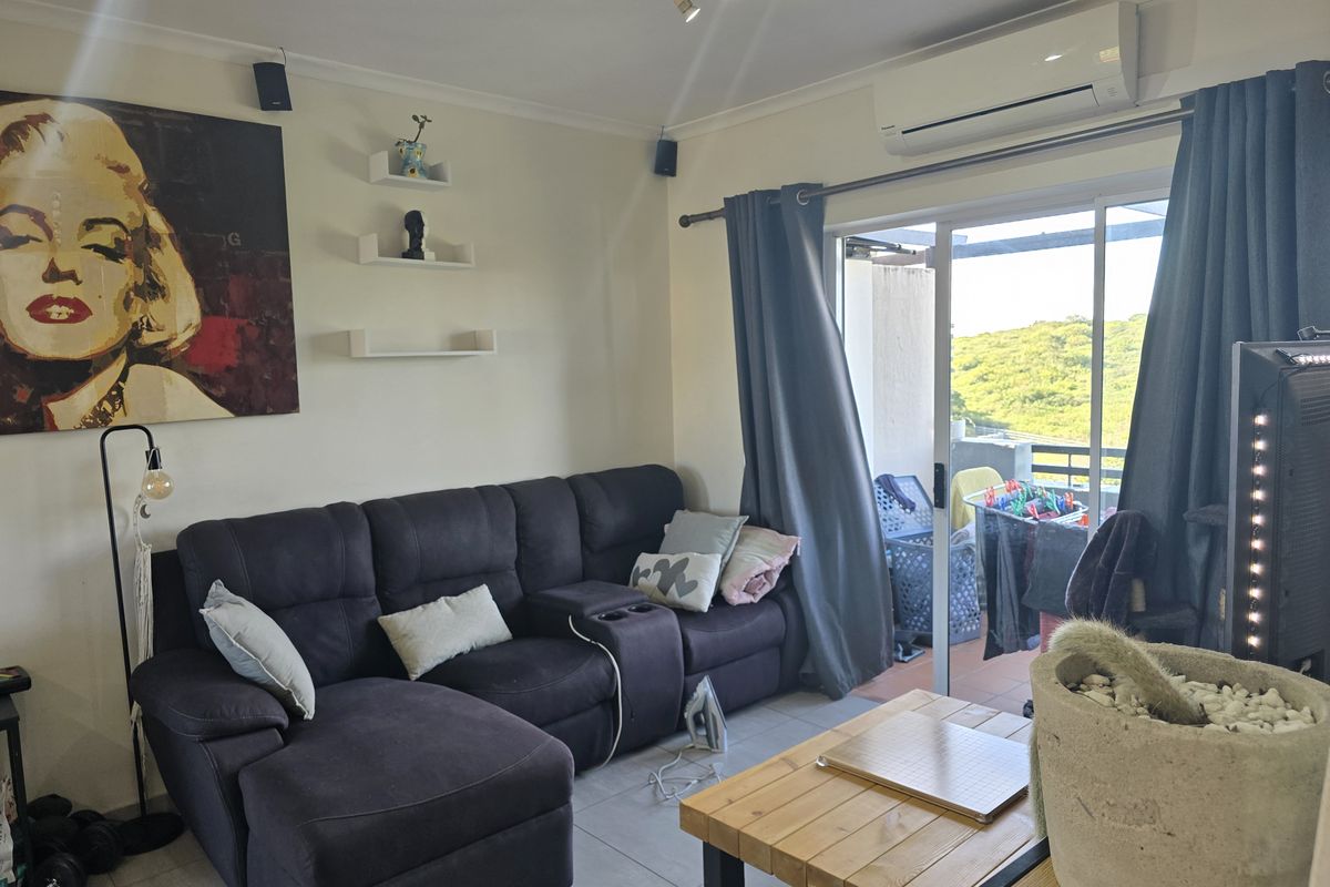 A comfortable living room featuring tiled flooring, a wall-mounted air conditioning unit, and large sliding glass doors providing access to an outdoor balcony area.