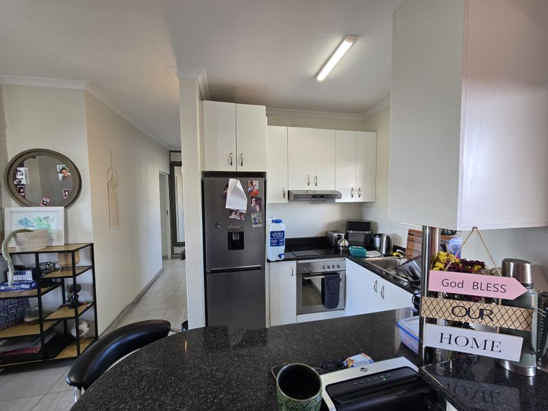 Compact kitchen featuring white cabinetry, granite countertops, and integrated stainless steel appliances, opening into a tiled hallway area.