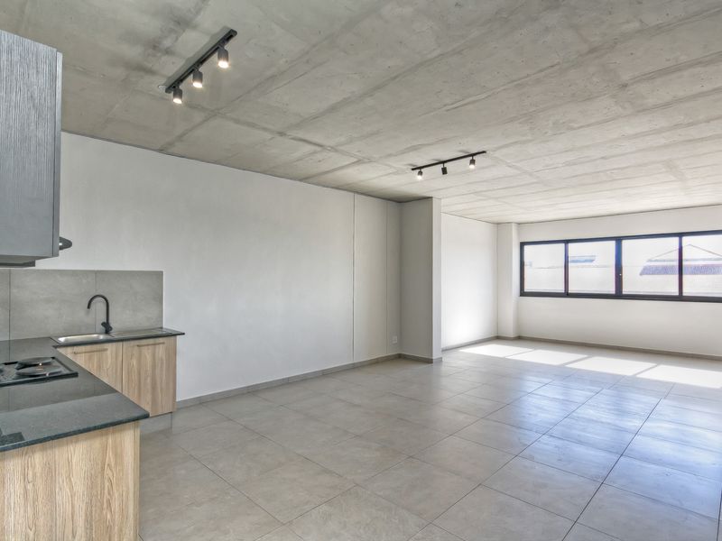 Modern open-plan living area featuring an exposed concrete ceiling, tiled floors, and a compact, contemporary kitchen with built-in cabinetry and stone countertops.
