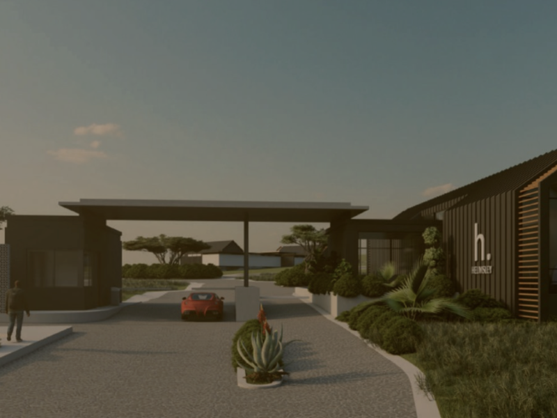 A modern residential estate entrance featuring a sleek gatehouse, paved driveway, and contemporary architectural design with landscaped surroundings.