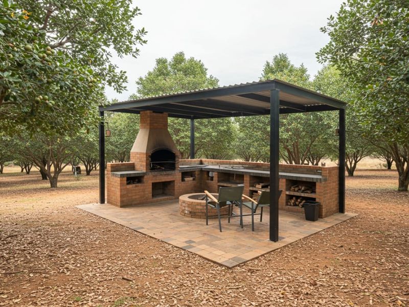 An outdoor entertainment area featuring a built-in brick braai, fire pit, and covered patio structure set within a landscaped orchard.