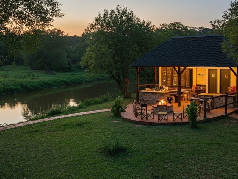 A scenic riverside covered patio featuring stone masonry, built-in braai facilities, and timber structural elements, set within a tranquil natural landscape.
