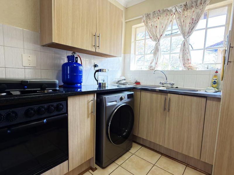 Compact kitchen featuring light wood-finish cabinetry, dark countertops, tiled backsplash, built-in oven, and integrated laundry appliance space.