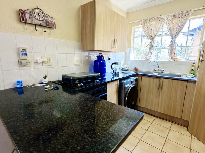 A functional kitchen featuring granite countertops, light wood cabinetry, tiled backsplash, and integrated laundry facilities with a window overlooking the exterior.