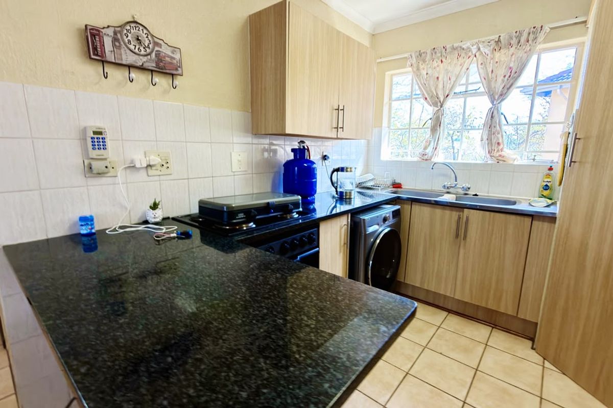 A functional kitchen featuring granite countertops, light wood cabinetry, tiled backsplash, and integrated laundry facilities with a window overlooking the exterior.