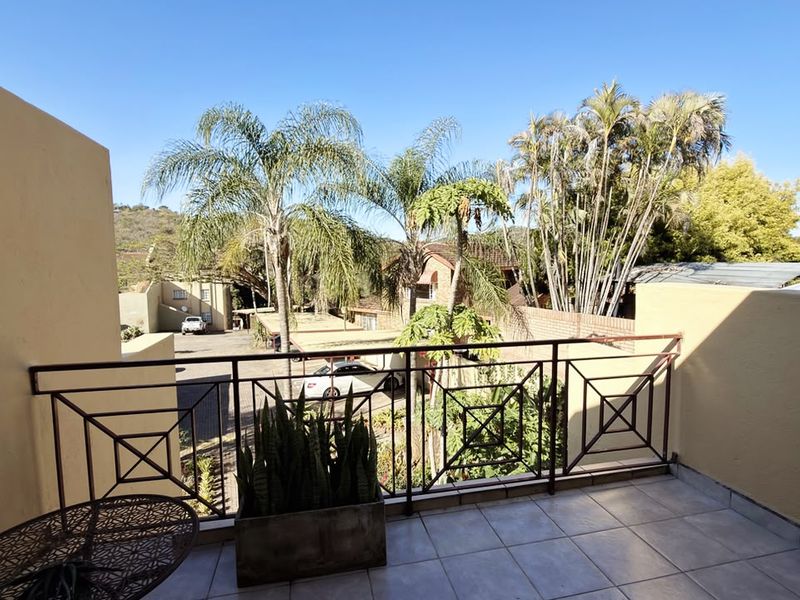 A private balcony featuring tiled flooring and a decorative metal balustrade, offering an open view of the surrounding complex and greenery.