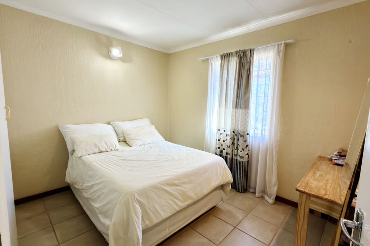 A functional bedroom featuring tiled flooring, neutral wall finishes, and a window with security bars, providing a simple and practical living space.