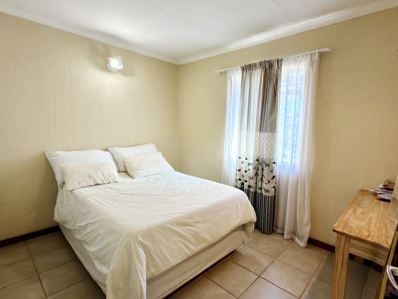 A functional bedroom featuring tiled flooring, neutral wall finishes, and a window with security bars, providing a simple and practical living space.