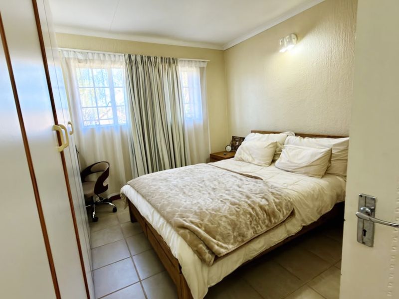 A functional bedroom featuring built-in cupboards, tiled flooring, and a wall-mounted light fixture, offering a neutral and practical living space.