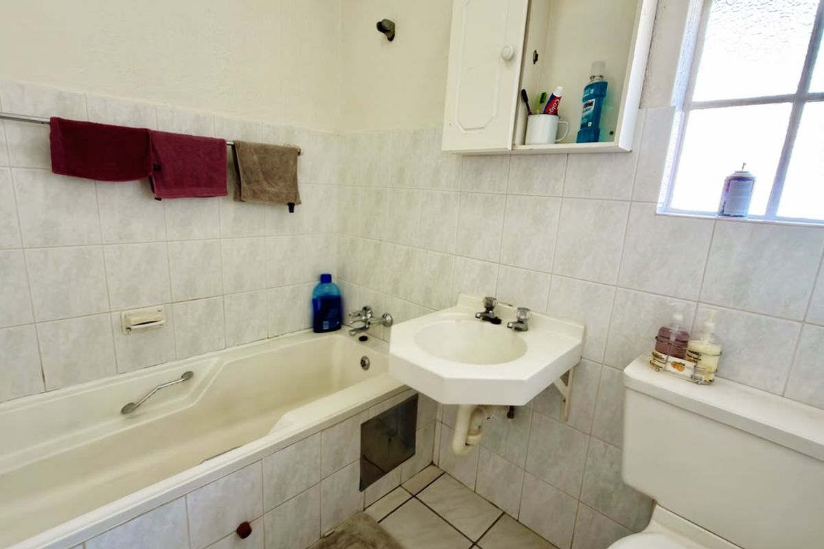 A functional bathroom featuring a bathtub, wall-mounted basin, and toilet with tiled finishes, offering potential for modernization and cosmetic updates.
