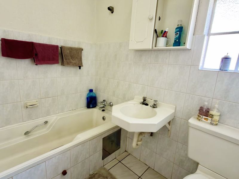 A functional bathroom featuring a bathtub, wall-mounted basin, and toilet with tiled finishes, offering potential for modernization and cosmetic updates.