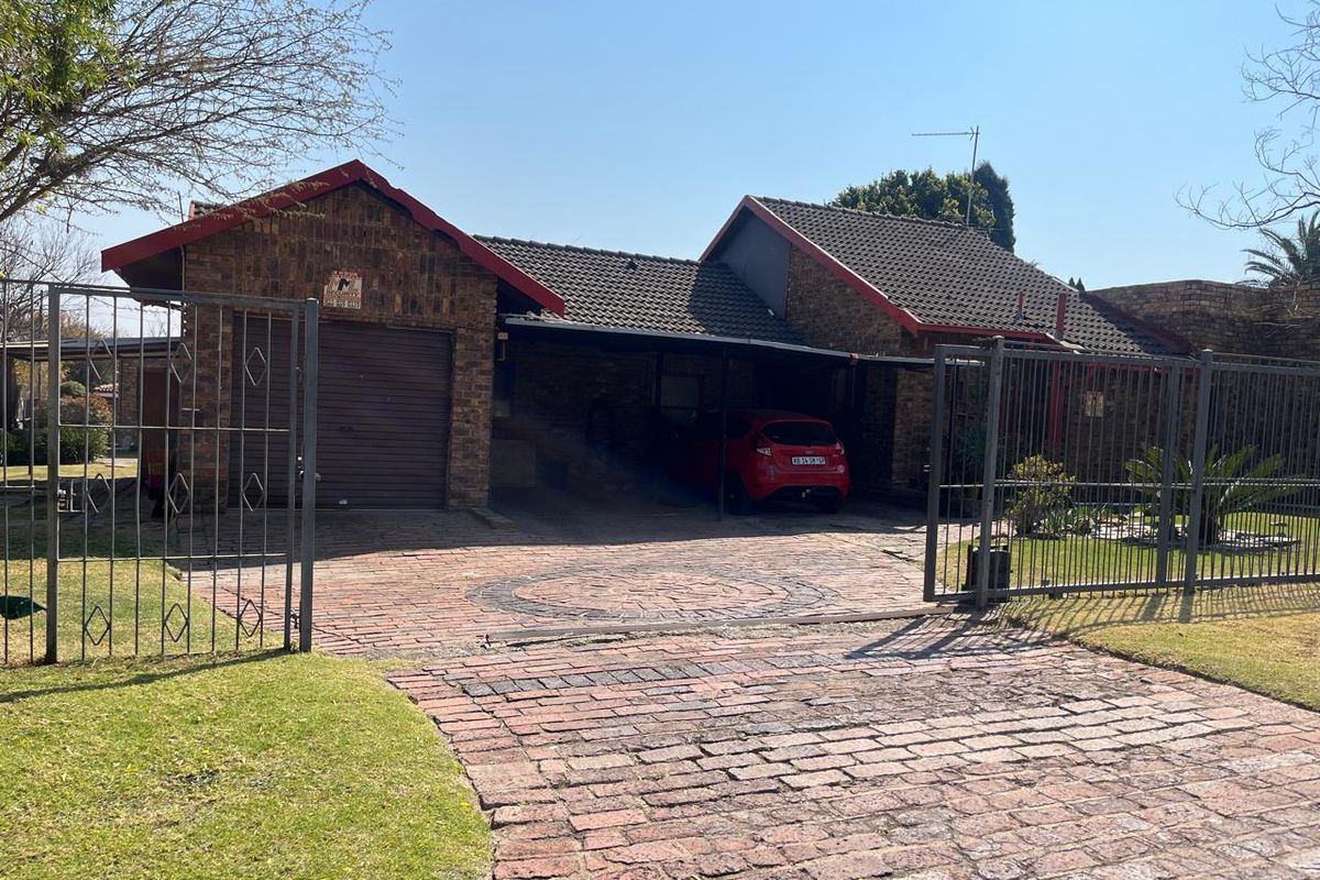 Front view of a face brick house featuring a paved driveway, secure metal gate, single garage, and a covered carport area.
