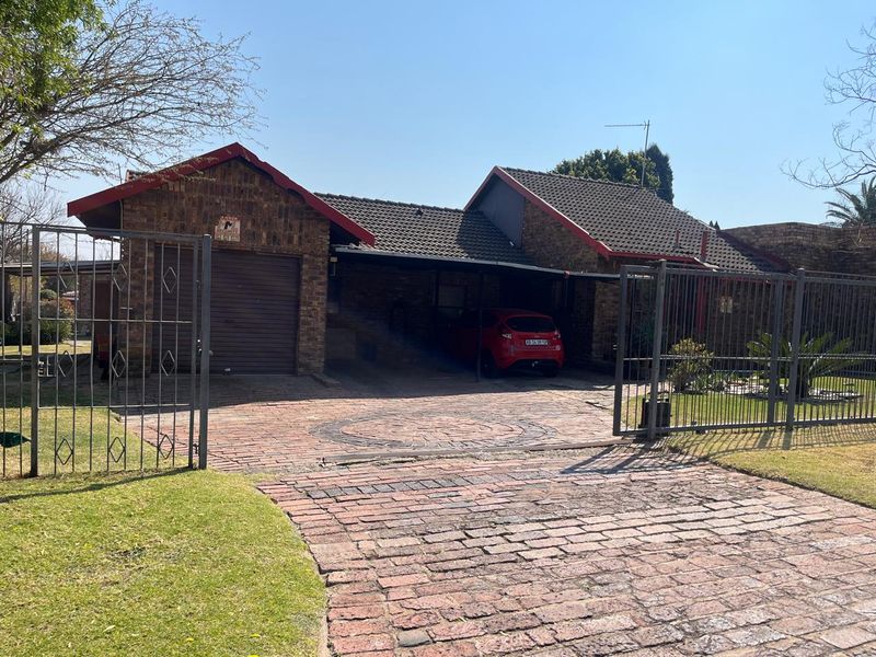 Front view of a face brick house featuring a paved driveway, secure metal gate, single garage, and a covered carport area.