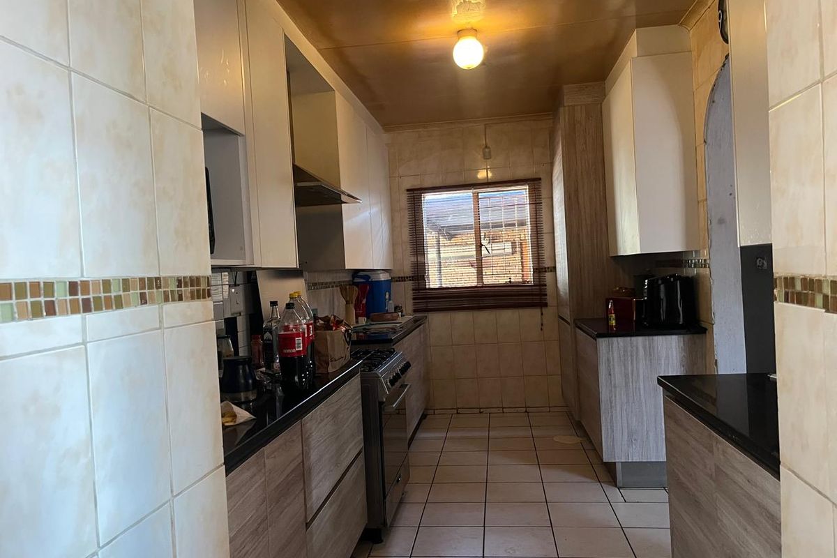A functional galley-style kitchen featuring built-in cabinetry, granite countertops, a gas stove with extractor fan, and tiled finishes throughout.