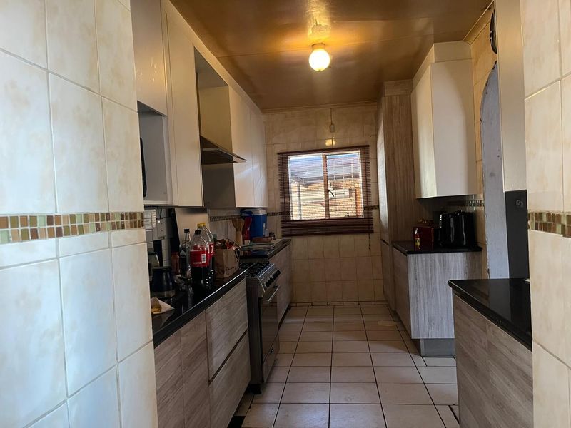 A functional galley-style kitchen featuring built-in cabinetry, granite countertops, a gas stove with extractor fan, and tiled finishes throughout.