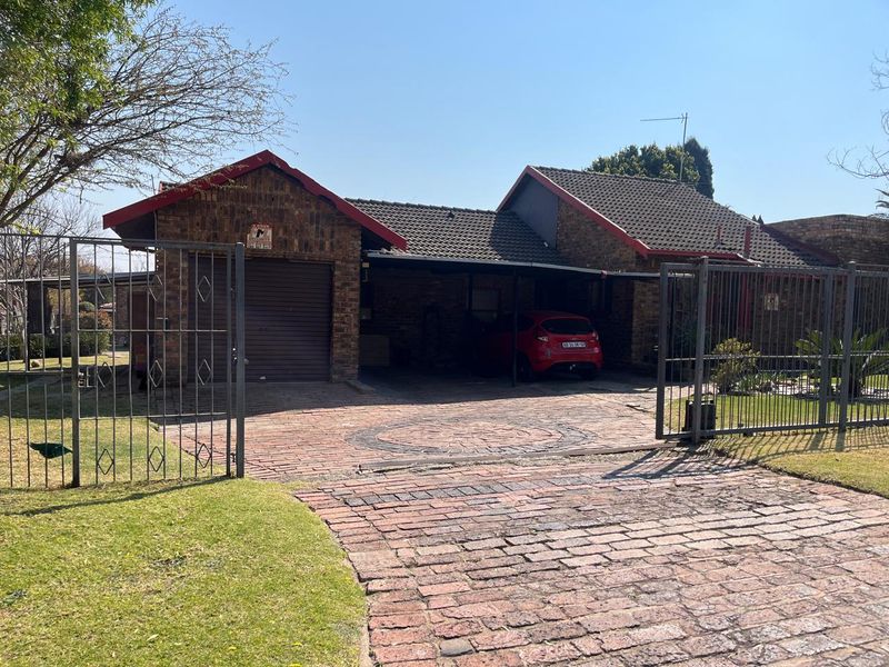 Front view of a brick house featuring a paved driveway, secure metal gate, integrated garage, and a covered carport area.
