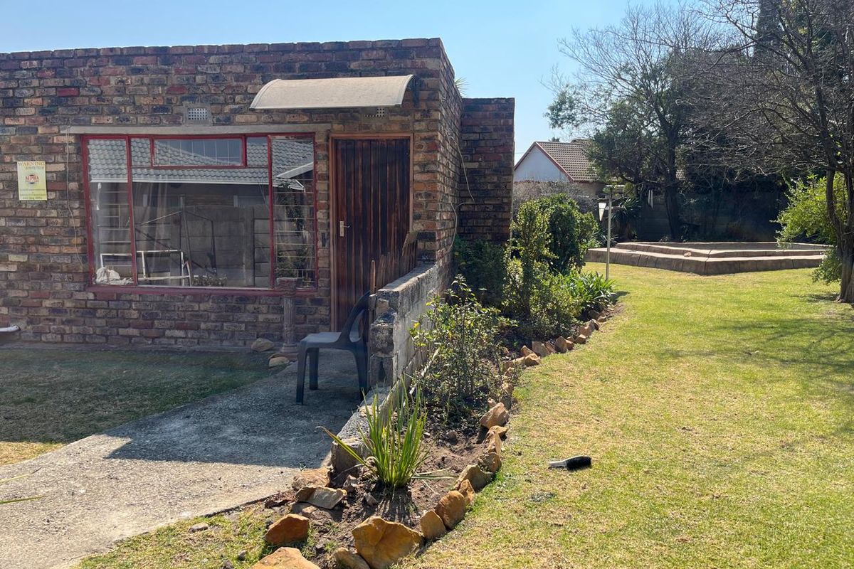 Rear view of a face brick house featuring a concrete pathway, established garden beds, and a lawn area.