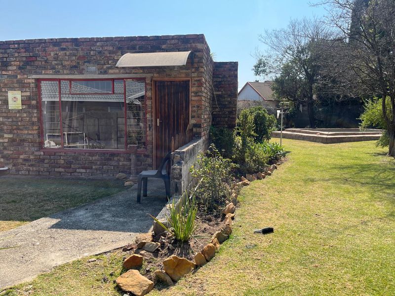 Rear view of a face brick house featuring a concrete pathway, established garden beds, and a lawn area.