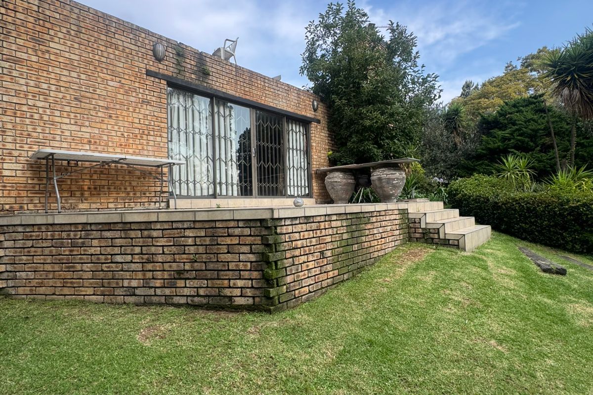 Rear view of the property featuring a raised brick patio, sliding glass doors with security gates, and a well-maintained lawn area.