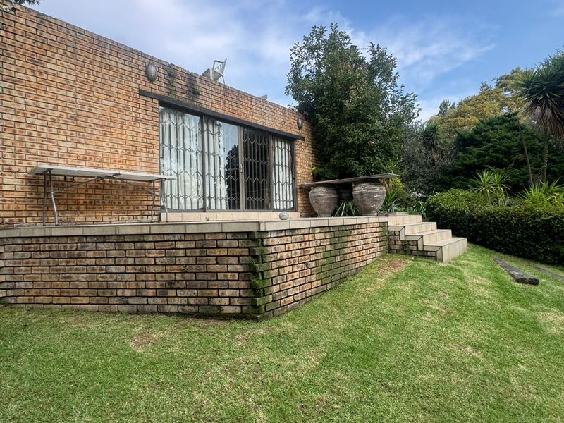 Rear view of the property featuring a raised brick patio, sliding glass doors with security gates, and a well-maintained lawn area.