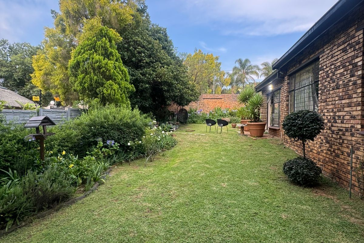 A well-maintained rear garden featuring a lush green lawn, established garden beds, and a classic face-brick exterior wall of the house.