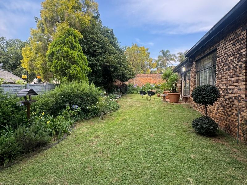 A well-maintained rear garden featuring a lush green lawn, established garden beds, and a classic face-brick exterior wall of the house.