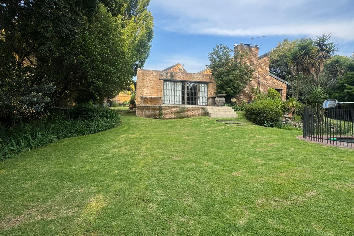 Rear view of a brick house featuring a raised patio, sliding glass doors, and a spacious garden with a pool area.