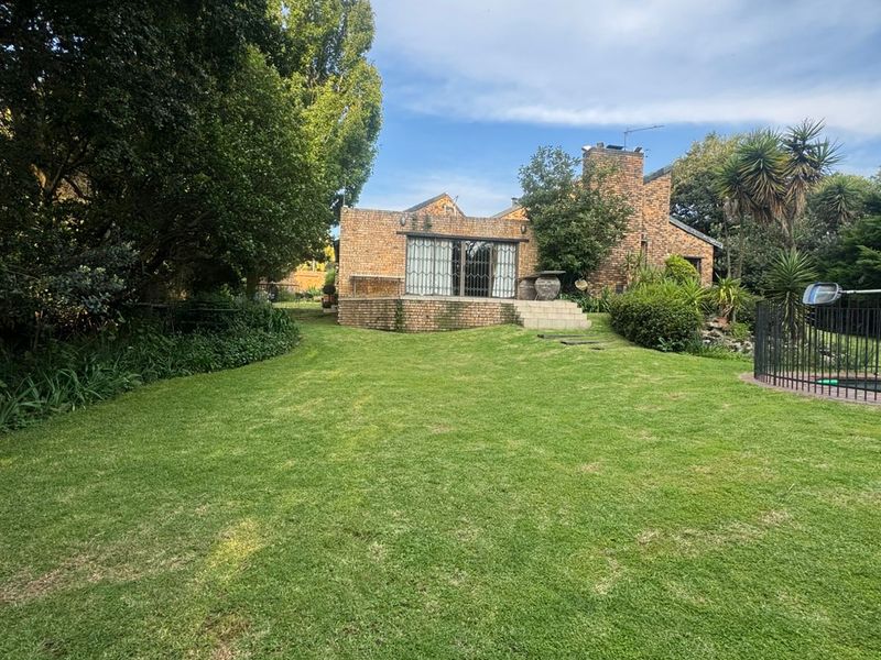 Rear view of a brick house featuring a raised patio, sliding glass doors, and a spacious garden with a pool area.