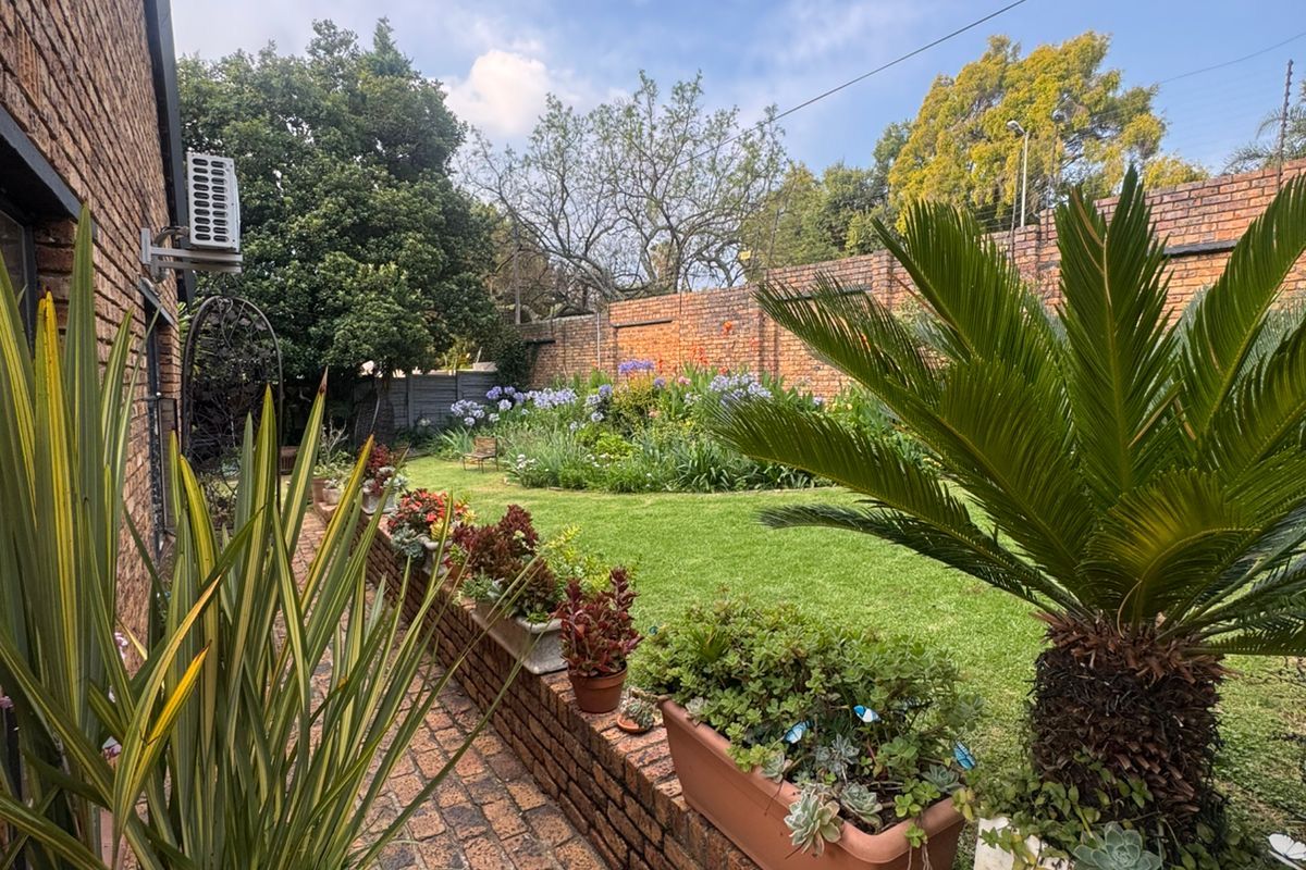 A well-maintained rear garden featuring a brick paved pathway, brick retaining walls, established lawn, and perimeter brick boundary walling.
