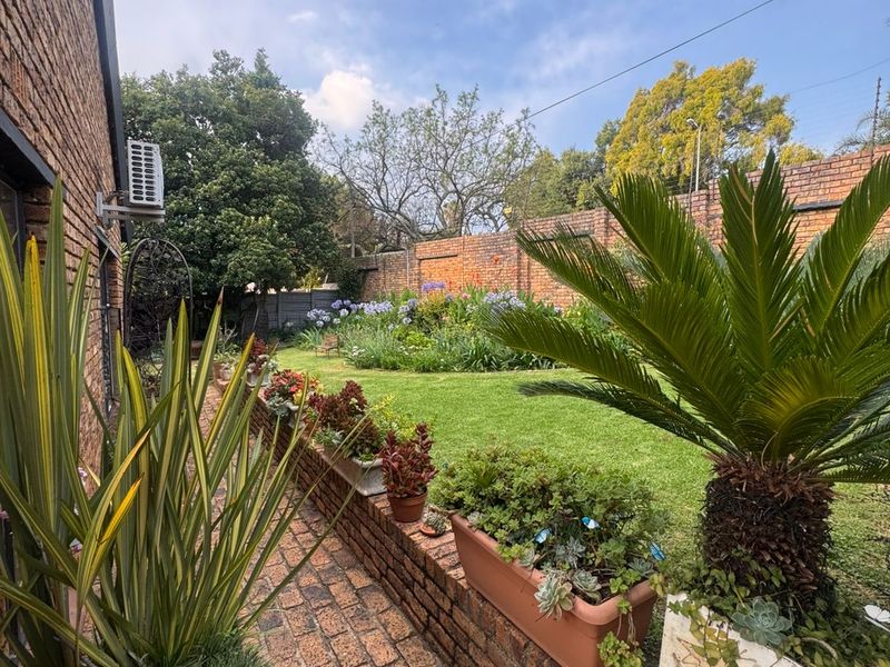 A well-maintained rear garden featuring a brick paved pathway, brick retaining walls, established lawn, and perimeter brick boundary walling.