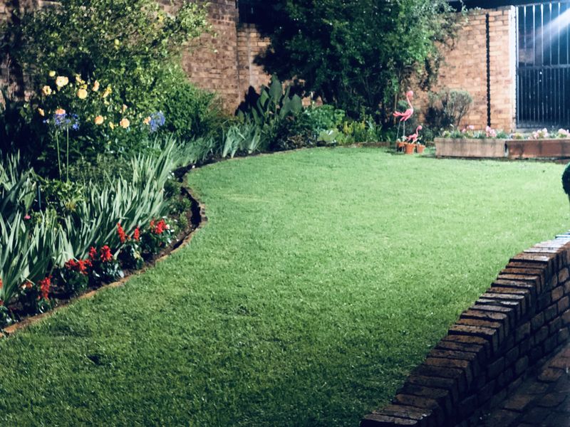 A well-maintained private garden featuring a lush green lawn, established garden beds, and solid brick boundary walls.