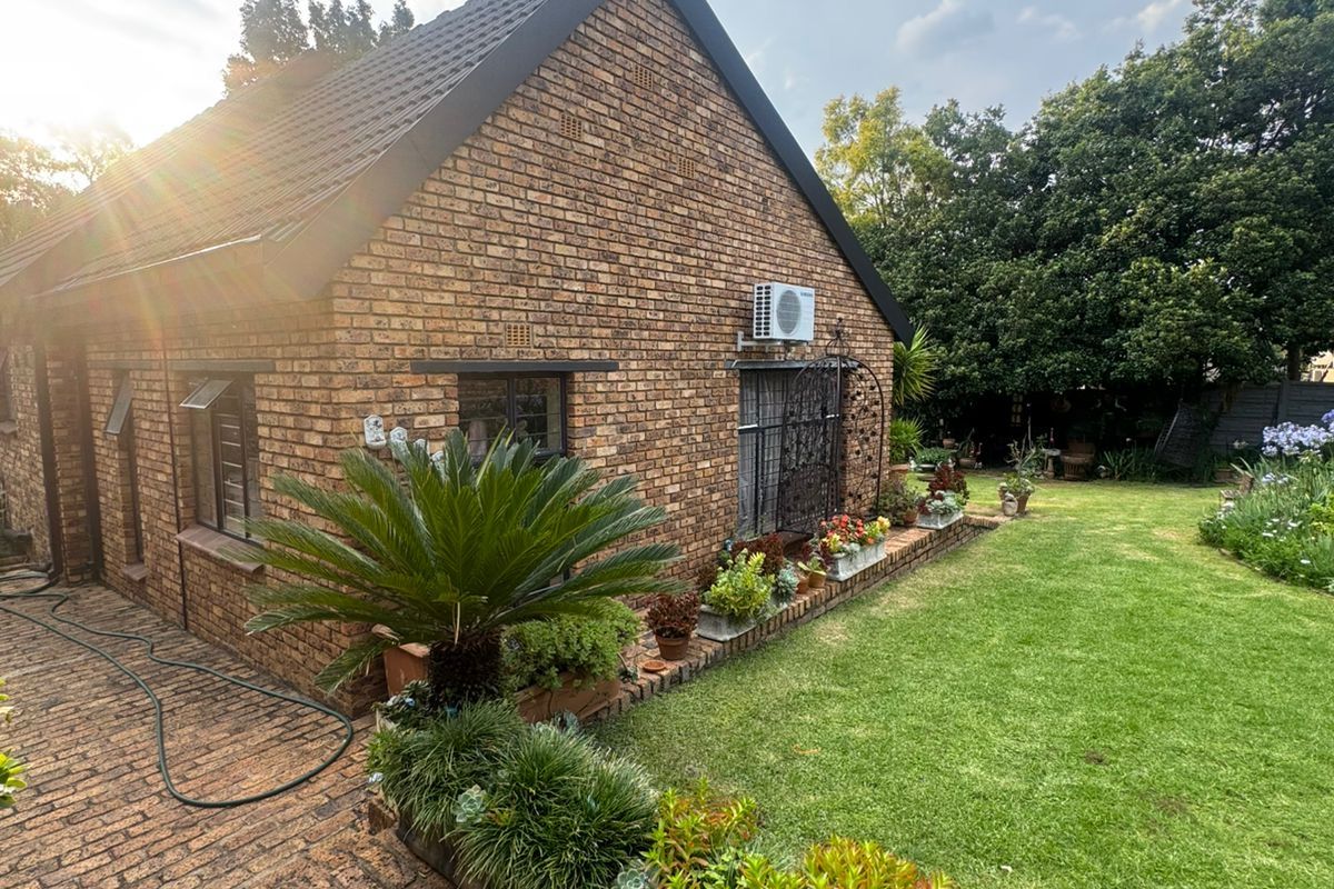 A well-maintained rear exterior view of a face brick house featuring a paved walkway, established garden, and an external air conditioning unit.