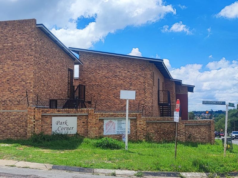 Street-level view of the Park Corner apartment complex, featuring face brick construction, perimeter security walls, and external metal staircases.