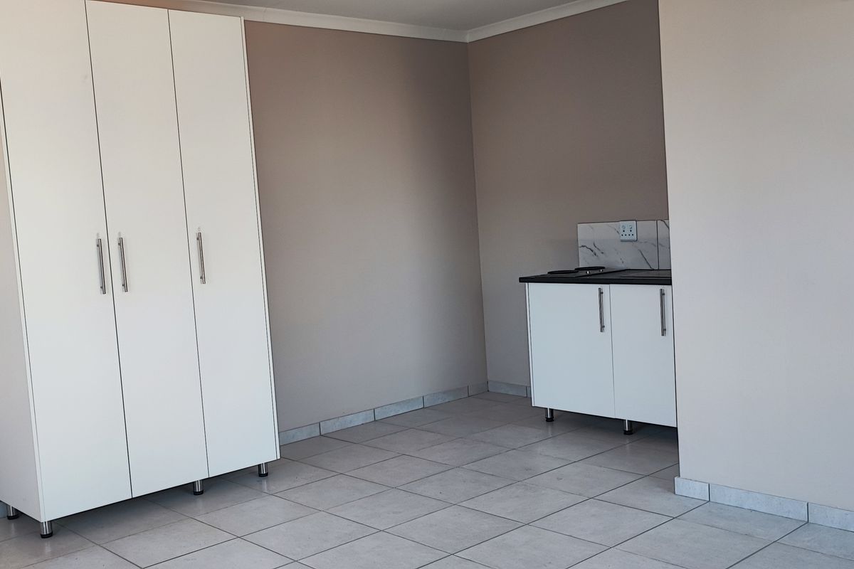 A compact, empty kitchen area featuring white built-in cabinetry, tiled flooring, and a neutral wall finish, suitable for a small apartment layout.