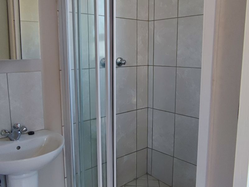 A functional bathroom featuring a pedestal basin, a tiled shower enclosure, and an electric water heater.