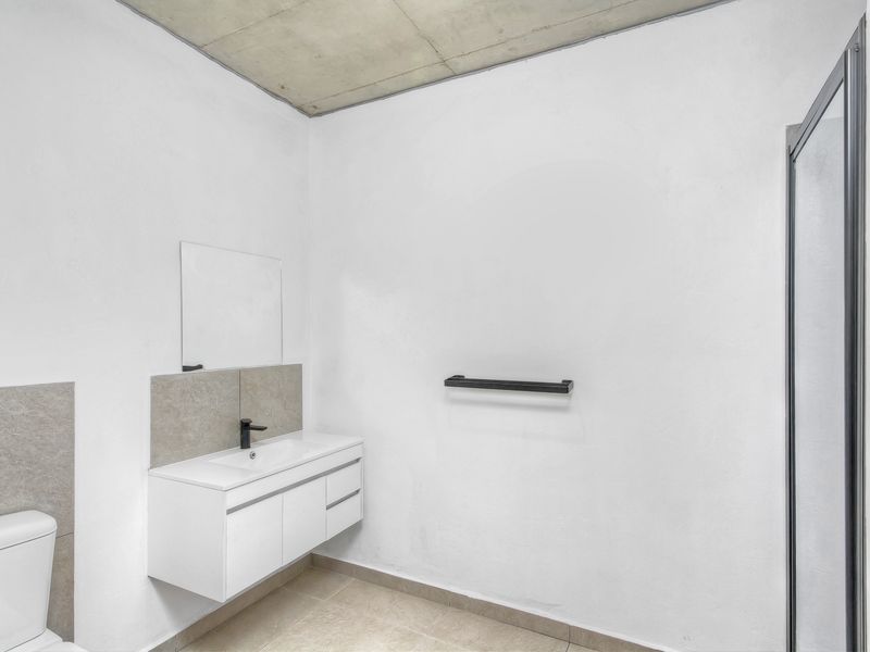 Modern bathroom featuring a wall-mounted vanity, black fixtures, a shower enclosure, and an exposed concrete ceiling, presenting a clean and contemporary aesthetic.
