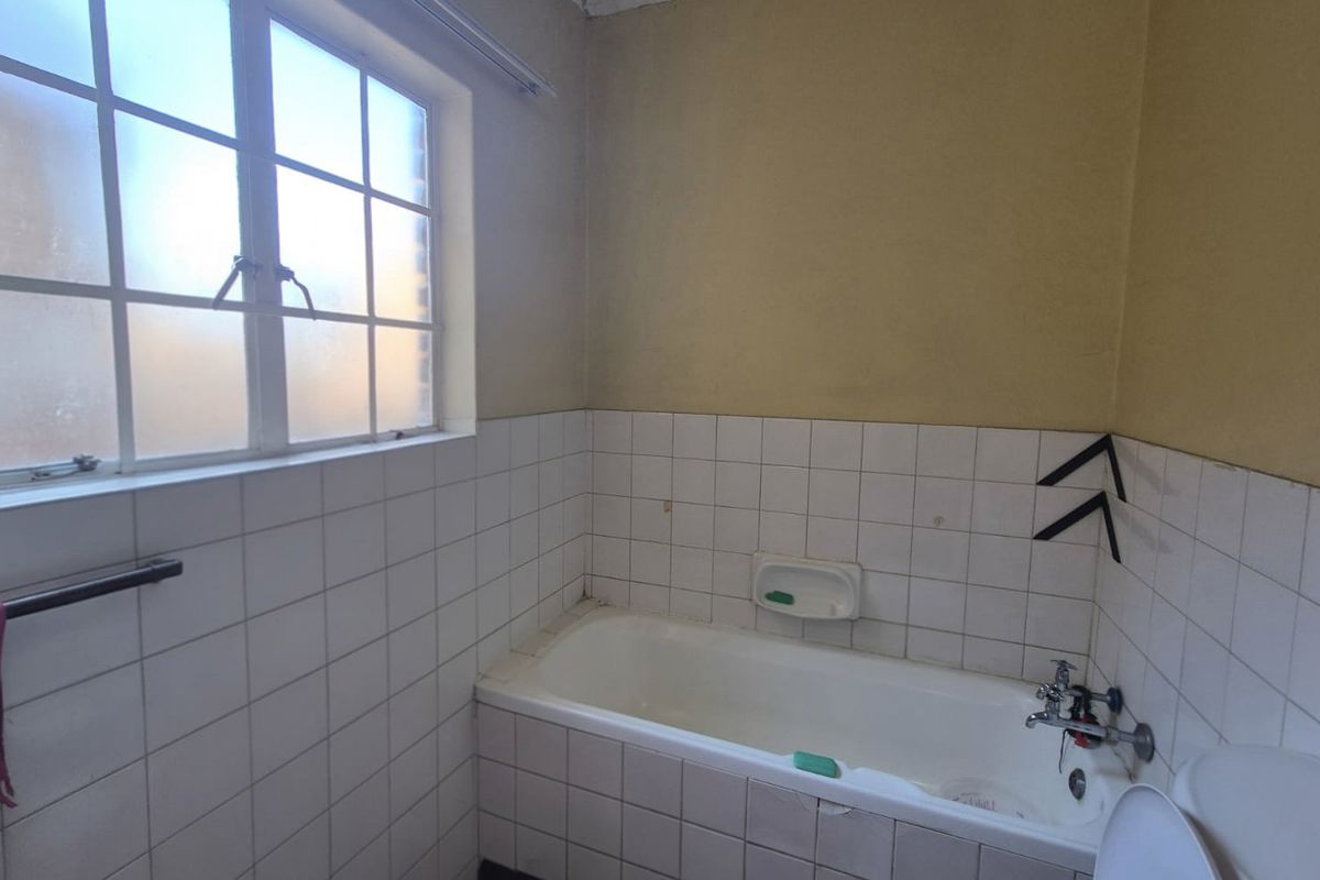 A dated bathroom featuring a standard bathtub with tiled splashback and a window, requiring cosmetic updates to modernize the space.