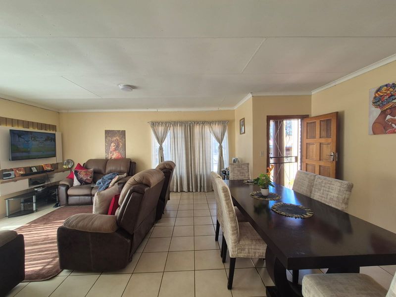 Open-plan living and dining area featuring tiled flooring, timber paneling, and direct access to the exterior via a security gate and timber door.