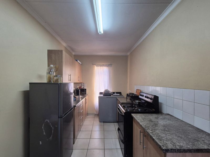 A functional galley-style kitchen featuring laminate cabinetry, granite-look countertops, tiled backsplash, and ceramic flooring, providing a practical workspace for daily meal preparation.
