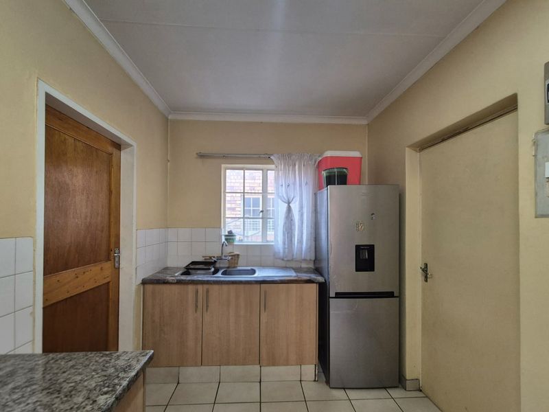 A compact kitchen featuring laminate cabinetry, a stainless steel sink, tiled splashbacks, and tiled flooring, offering a functional space with potential for modernization.
