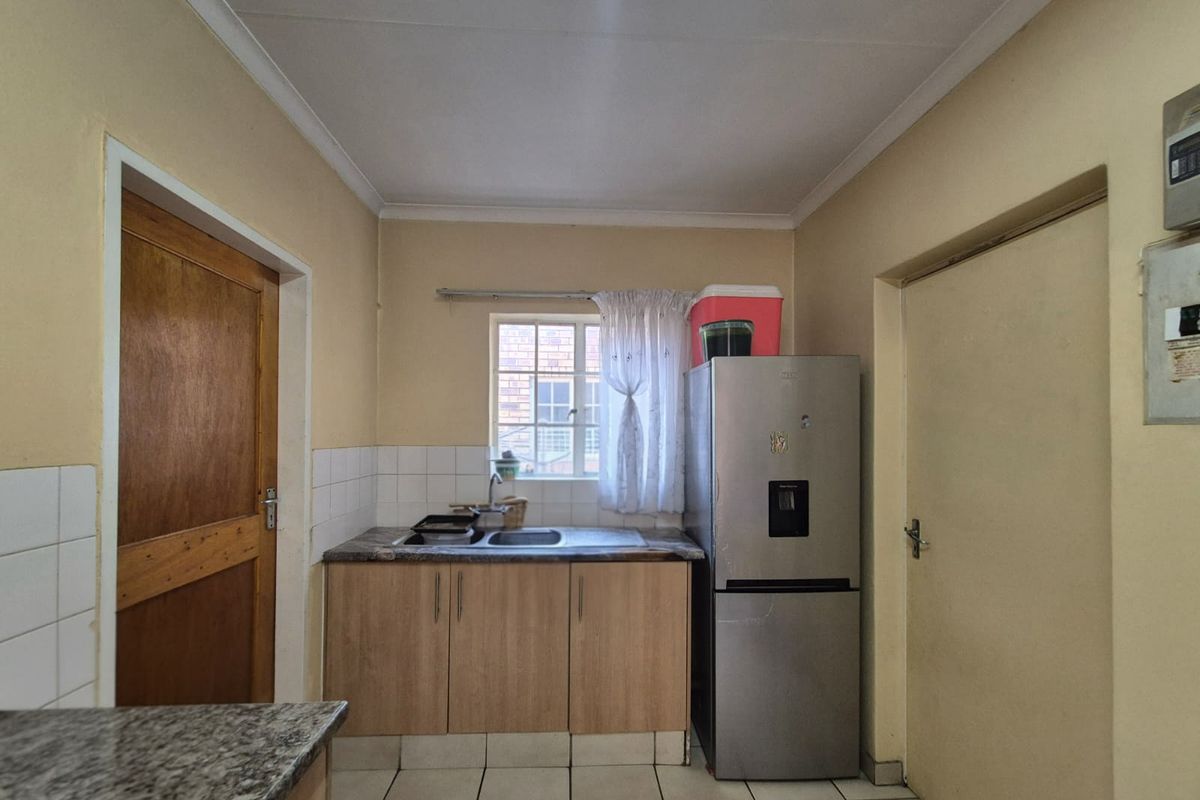 A compact kitchen featuring laminate cabinetry, a stainless steel sink, tiled splashbacks, and tiled flooring, offering a functional space with potential for modernization.